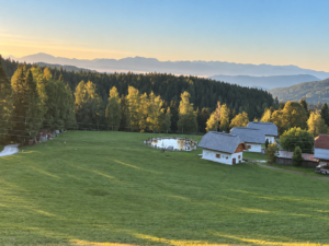 Drei Naturhäuser von Ebner 1822 in der Morgensonne mit Teich und Blick auf die Nockberge